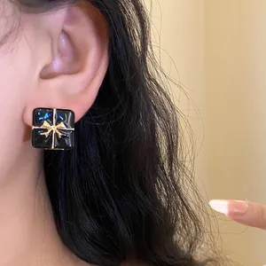 Close-up of elegant black square gift box earring with gold ribbon knot design on ear