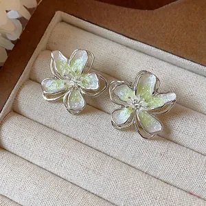 Close-up of elegant flower stud earrings featuring green gradient enamel and subtle glitter