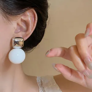 Primo piano di orecchini minimalisti a forma di quadrato e sfera in resina bianca su modella