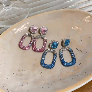 Detailed macro view of rhinestone hollow drop stud earrings in pink and blue on a plate