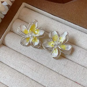 Macro view of dainty white and yellow drip oil flower stud earrings in jewelry tray