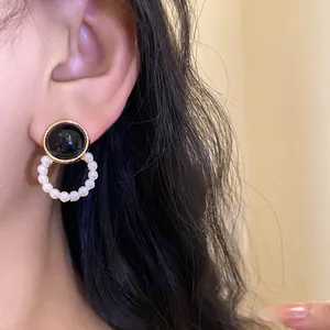 Close-up of elegant black stud earrings with a white pearl hoop dangle on ear