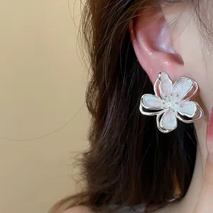 Close-up of elegant white enamel flower stud earring worn on ear