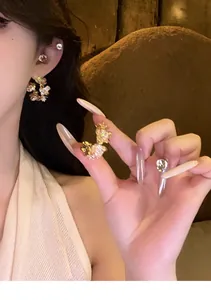 Close-up of elegant gold-tone zircon flower earrings worn and held by model