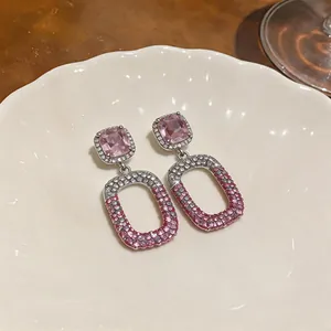 Elegant close-up of pink crystal drop earrings with pave diamonds on white ceramic plate