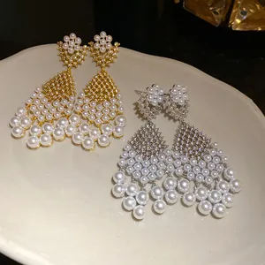 Close-up of elegant gold and silver chandelier earrings featuring pearls and zircons on a tray