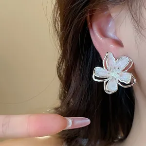 Detailed close-up showing elegant flower stud earrings with white enamel and glitter petals