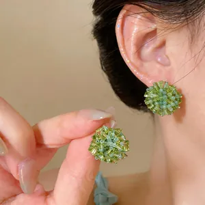 Handmade green glass flower stud earrings shown on ear and held in hand for detail