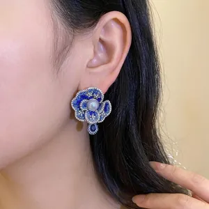 Elegant vintage blue crystal flower stud earrings with a central pearl worn by a model