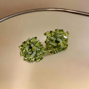 Detailed macro view of green glass floral stud earrings with intricate beadwork.