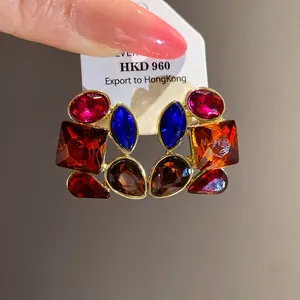 Detalle macro de pendientes vintage dorados con pedrería multicolor de varias formas