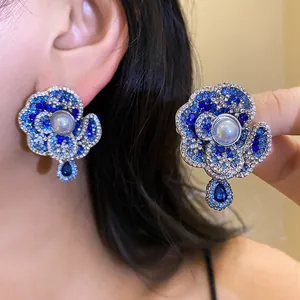 Close-up of vintage flower earrings with blue crystals and central pearl worn on ear