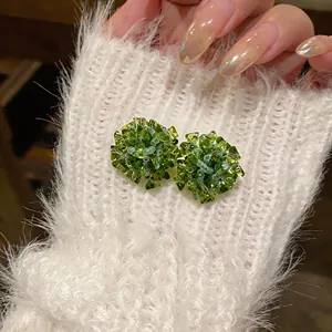 Close-up detail of handmade green glass flower stud earrings on white knit fabric