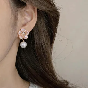 Close-up detail of a delicate pink flower earring with a pearl drop on model's ear