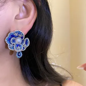 Close-up view of a vintage-style blue crystal flower earring with a pearl on a model