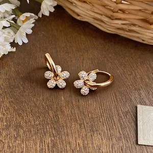 Eleganti orecchini a cerchio a fiore placcati oro 14k con zirconi su sfondo di legno.