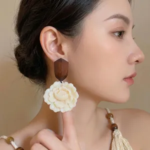 Elegant wood and cream resin flower stud earrings worn by a model in a lifestyle setting