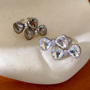 Detail view of iridescent and grey crystal bow-knot adjustable rings on ceramic plate.