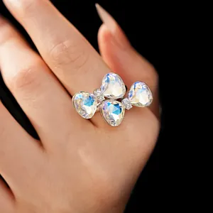 Detailed view of an elegant bow-shaped ring with iridescent crystals on a hand.