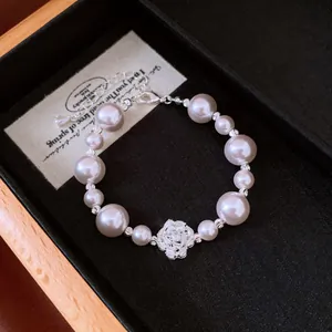 Close-up of an elegant pearl bracelet featuring a detailed sparkling zircon flower charm.