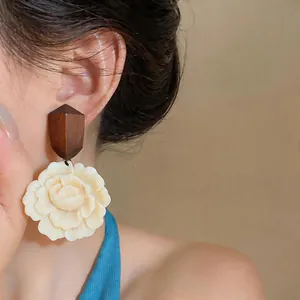 Close-up of elegant cream resin flower earrings with brown geometric wood studs detail