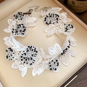 Close-up of a white lace choker necklace with black and white beaded flower patterns.