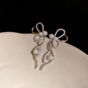 Dettaglio di orecchini a clip a fiocco con zirconi e perle su piatto di ceramica.