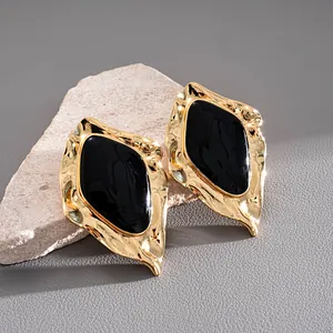 Nahaufnahme unregelmäßiger goldfarbener geometrischer Ohrringe mit schwarzer Emaille