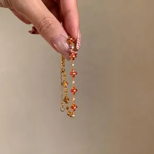 Detailed close-up of an elegant gold clover bracelet with orange and clear zircons