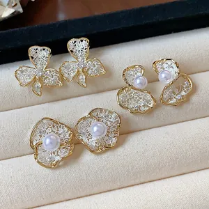 Detail shot of 18K gold plated floral pearl earrings with intricate lace metalwork design.