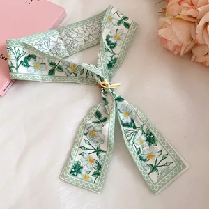 Detail view of a green floral print skinny silk scarf with a decorative yellow buckle