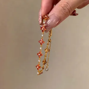 Close-up detail of a gold-tone lucky clover bracelet with orange and white cubic zircons.
