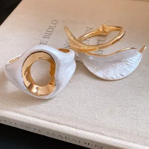 Macro detail of vintage gold-plated bangles with elegant white enamel and organic shapes