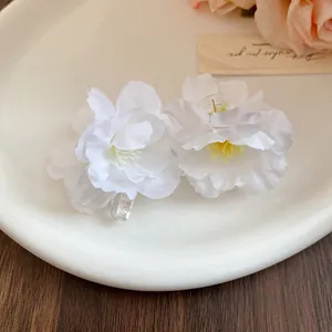Detailed close-up showing texture of white fabric flower hair clips with clear duckbill base