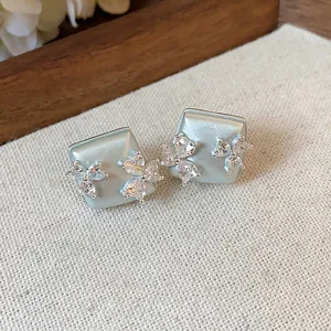 Close-up of pale blue geometric stud earrings with sparkling zircon floral patterns