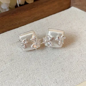 Close-up detail of geometric silver stud earrings with sparkling zircon flowers