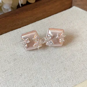 Close-up of rose gold square stud earrings with zirconia flower accents on linen.