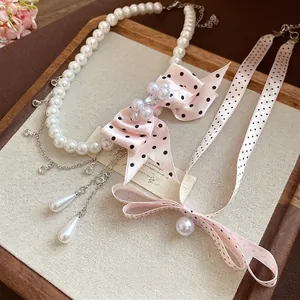Elegante collana di perle con fiocco di nastro a pois rosa e ciondoli a goccia.