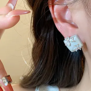 Close-up of geometric square stud earrings featuring sparkling zircon flower accents