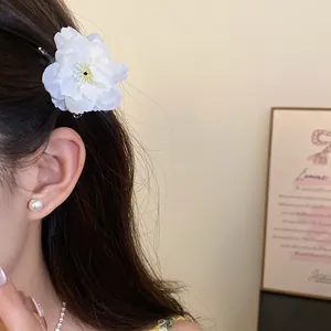 Macro view showing the delicate petals of a white fabric flower hair clip on dark hair
