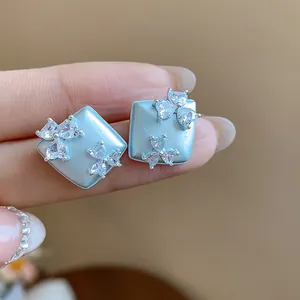 Close-up of light blue geometric stud earrings featuring sparkling zircon flower clusters