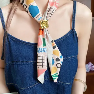 Close-up of printed silk scarf with gold square buckle on denim top