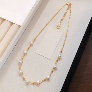 Detail view of a dainty French style pearl beaded necklace on a gold double chain