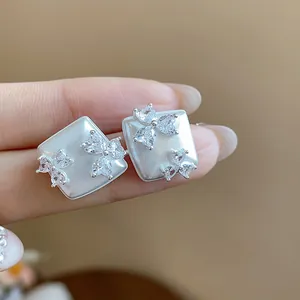 Close-up of square stud earrings with zircon heart flower details and pearly finish.