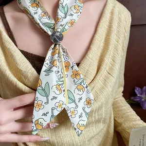 Detail of a floral print skinny scarf with a textured slide ring on a yellow sweater.