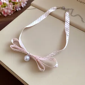 Primo piano di una collana a fiocco in nastro rosa a pois con pendente a perla bianca