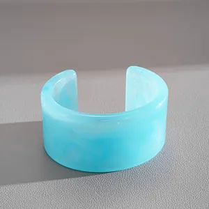 Dettaglio ravvicinato di un bracciale a polsino in resina marmorizzata blu chiaro minimalista