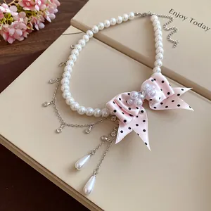 Dettaglio della collana di perle con fiocco rosa a pois e catenine argentate pendenti