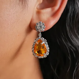 Close-up detail of luxury vintage teardrop earrings featuring a bright orange gemstone