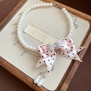 Dettaglio di un'elegante collana di perle con fiocco rosa a pois e ciondoli in cristallo.